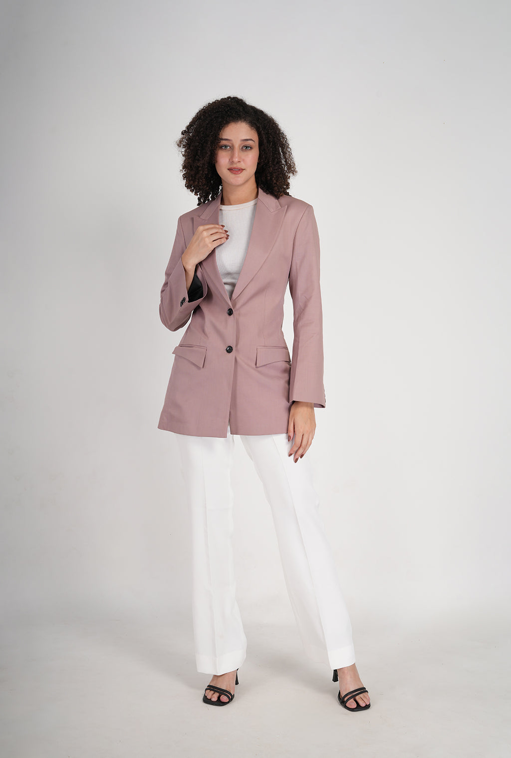 Woman wearing a pink blazer and white pants on a white background