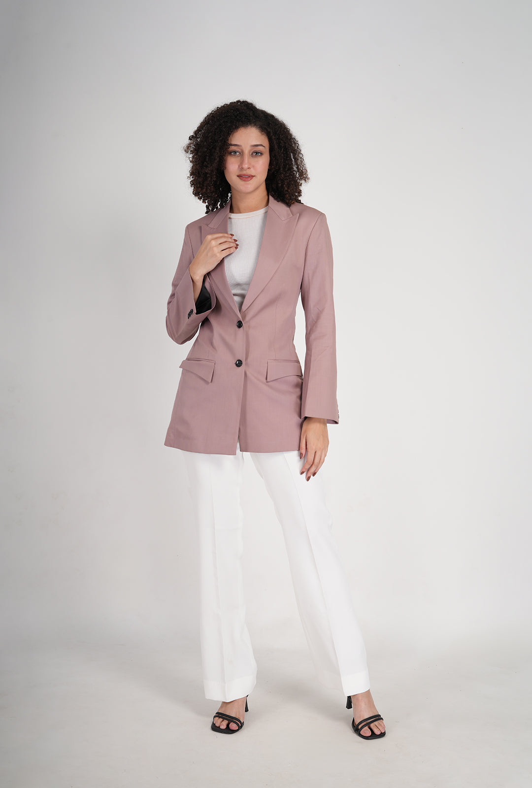 Woman wearing a pink blazer and white pants on a white background