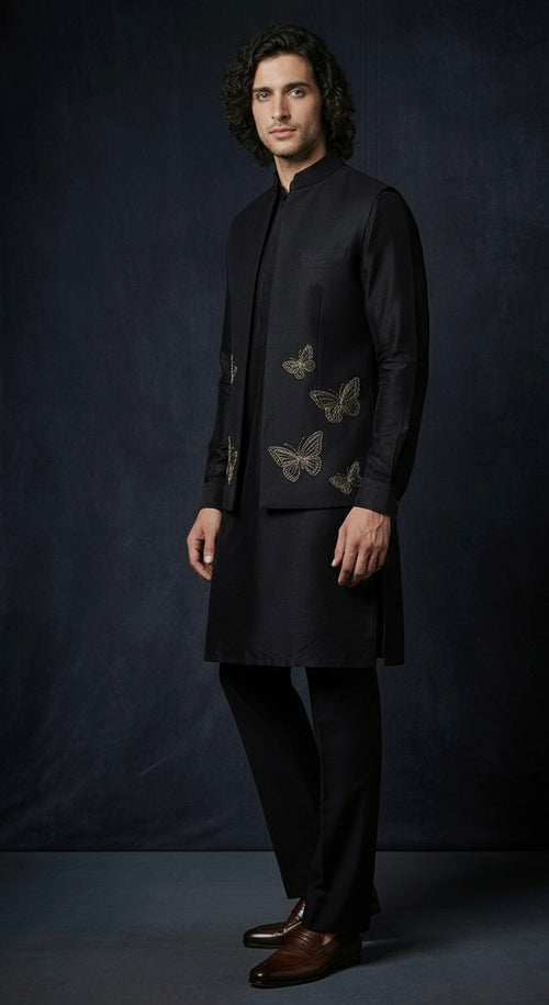 Man wearing a black embroidered kurta with butterfly designs against a dark background