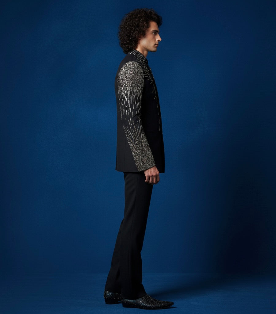 Man wearing a black suit with intricate patterns on a blue background