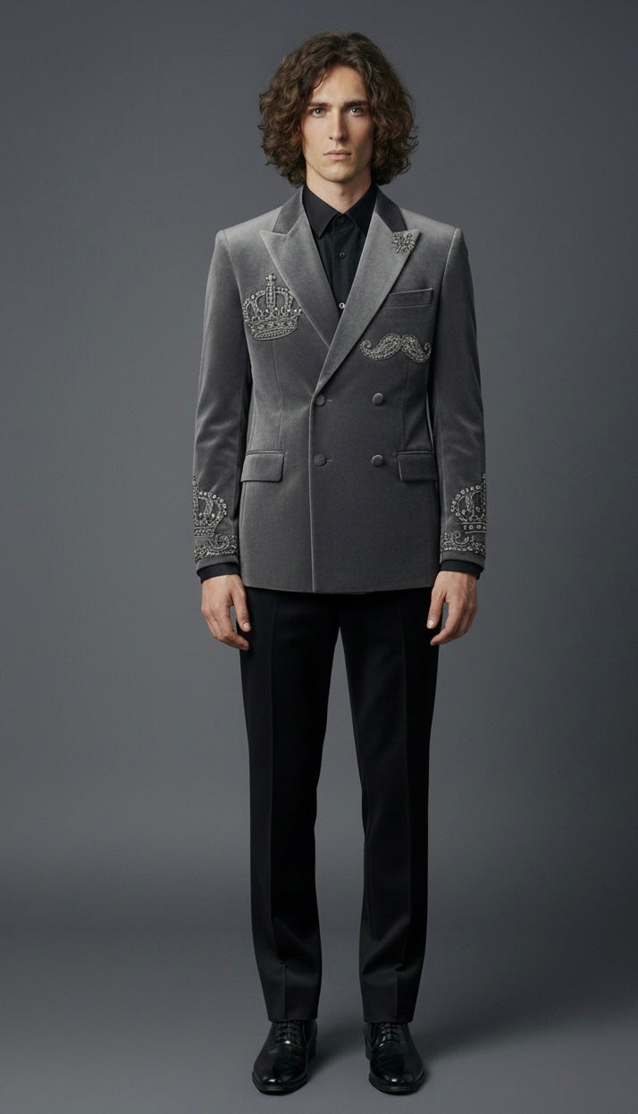Man wearing a gray embroidered blazer and black pants on a gray background