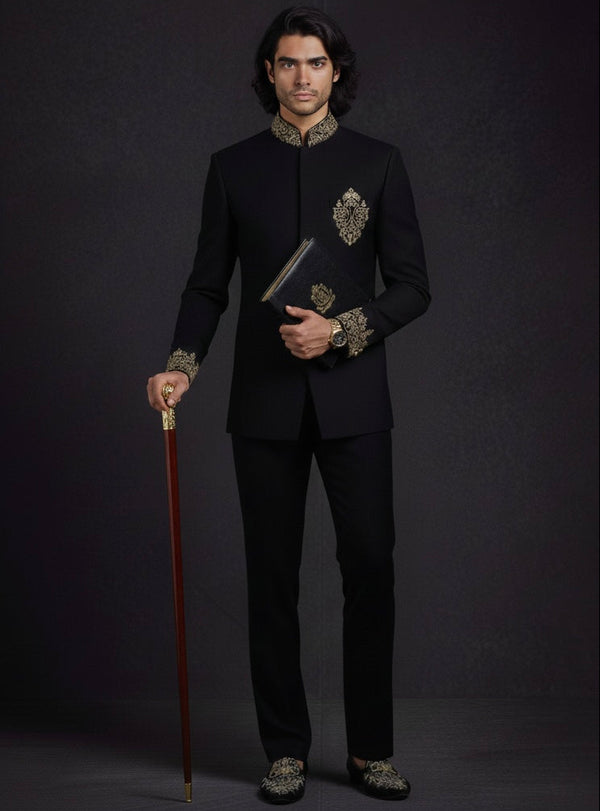 Man in a black embroidered suit holding a cane against a dark background