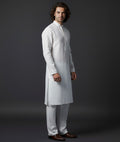 Man wearing a white kurta with white pants on a dark background