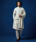 Man wearing a traditional cream kurta with floral patterns against a blue background