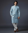 Man wearing a light blue sherwani with white pants on a dark gray background