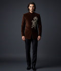 Man wearing a brown velvet suit with embroidery on a dark background