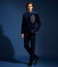 Man wearing a dark blue suit with an embroidered design on a blue background