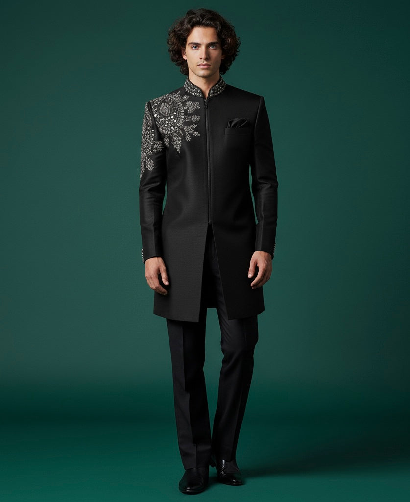 Man wearing a black sherwani with intricate embroidery on a green background