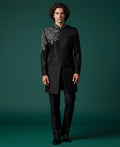 Man wearing a black sherwani with intricate embroidery on a green background