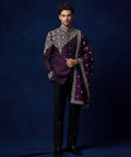 Man wearing a purple embroidered traditional outfit against a dark blue background