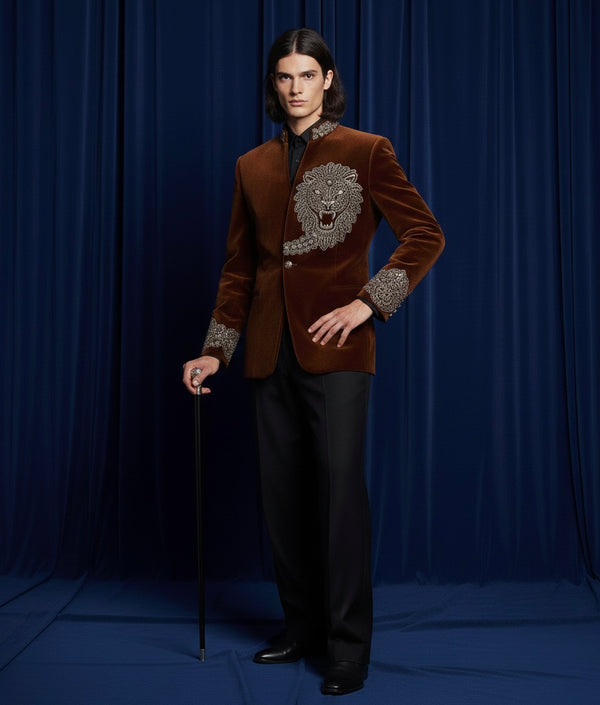 Man wearing a brown velvet blazer with a lion emblem against a blue curtain background
