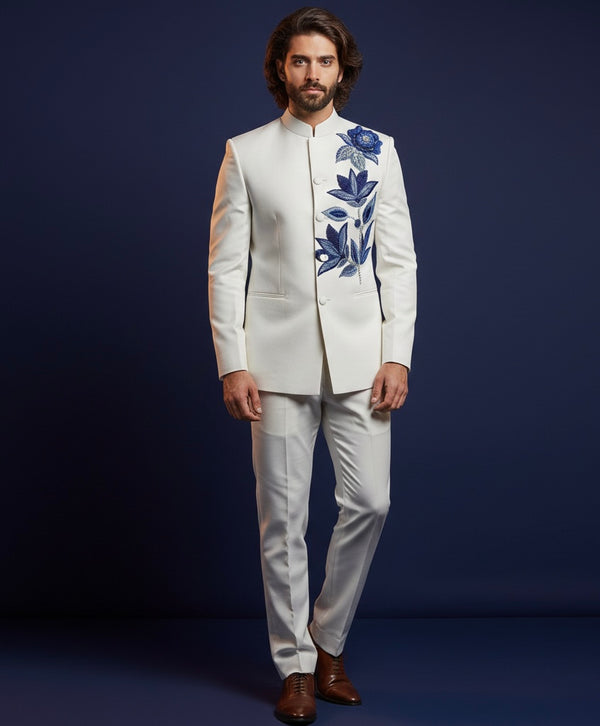 Man wearing a white suit with blue floral embroidery on a dark blue background