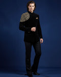 Man wearing a black suit with gold embroidery on a blue background
