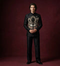 Man wearing a black embroidered suit against a dark red background