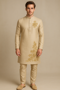 Man wearing a beige embroidered kurta with gold patterns on a beige background